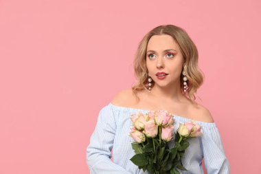 Pembe arka planda bir buket güzel gülleri olan güzel genç bir kadın.