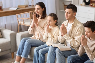 İncil 'i olan bir aile evdeki kanepede dua ediyor.