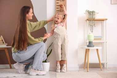 Genç anne, evdeki ahşap stadyumun yanında kızının boyunu ölçüyor.