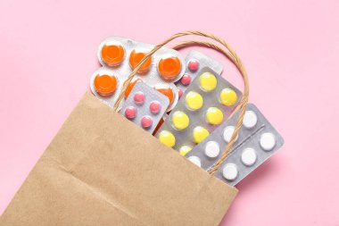 Pembe arka planda farklı haplarla dolu bir alışveriş torbası.