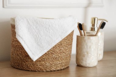 Hasır sepette havlu ve banyoda beyaz duvarın yanında diş fırçası.
