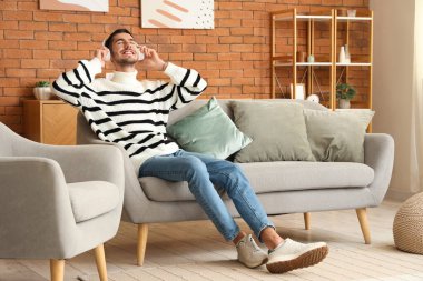 Kulaklıklı yakışıklı genç adam evdeki kanepede dinleniyor ve müzik dinliyor.