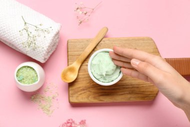 Kadın eli, bir kase vücut fırçası, deniz tuzu ve pembe arka planda temiz havlu, yakın plan.