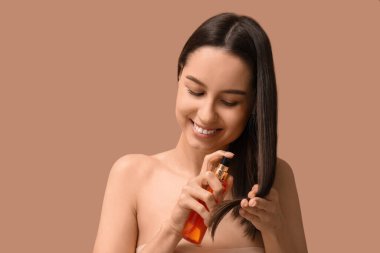 Bej arka planda saç tedavisi için kozmetik ürünleri olan genç bir kadın.