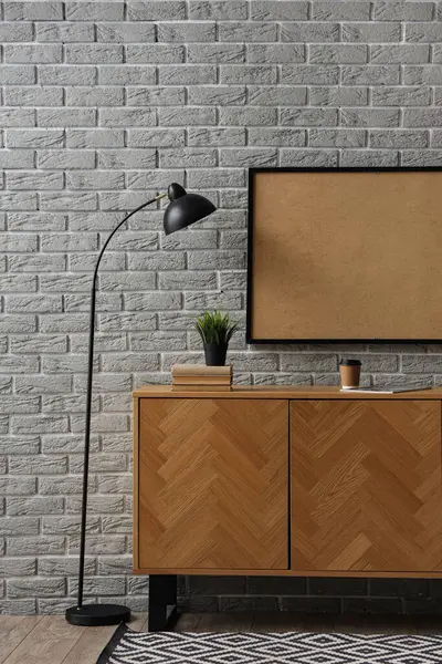 Çerçeveli ahşap dolap ve gri tuğla duvarın yanında lamba.