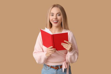 Kahverengi arkaplan üzerine kitabı olan güzel, mutlu bir kadın.