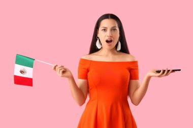 Pembe arka planda Meksika bayrağı ve cep telefonu olan şaşırmış genç bir kadın.