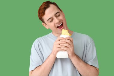 Genç adam yeşil arka planda lezzetli sandviçler yiyor.