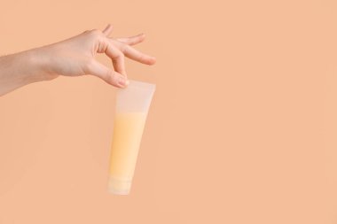 Arka planda doğal krem tüpü olan kadın eli, yakın plan.