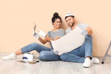 Bej duvarın yanında renk paleti olan genç ve güzel bir çift yeni evde tamirat yapıyor.