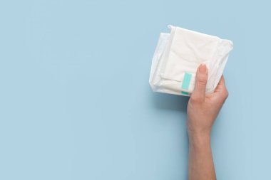 Mavi arka planda adet pedleri olan bir kadın el.