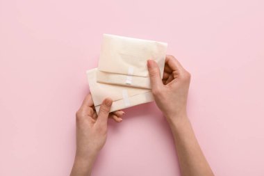 Pembe arka planda adet pedleri olan kadın elleri.