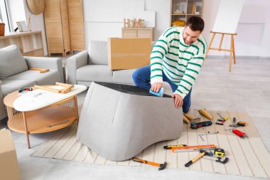 Zımba zımbalı genç adam evinde koltuk monte ediyor.