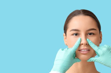 Cerrah, mavi arka planda estetik ameliyattan önce kadının burnuna dokunuyor.