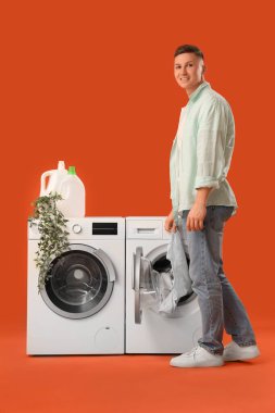 Yakışıklı genç adam çamaşır makinesini turuncu arka planda yıkıyor.