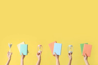 Kum saati tutan kadın eller ve sarı arka planda kitaplar.