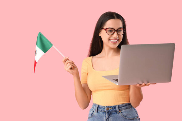 Young woman with Mexican flag and laptop on pink background