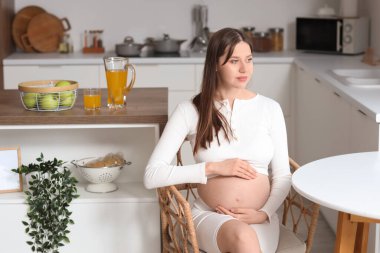 Genç hamile kadın mutfakta oturuyor.