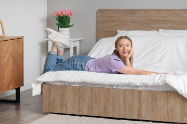 Güzel genç bir kadın yatak odasında rahat bir yatakta yatıyor.