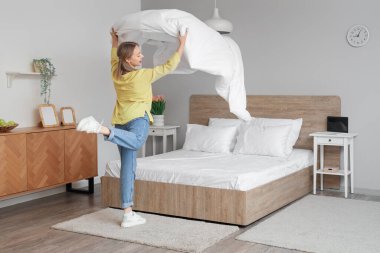 Modern yatak odasında yatağını yapan neşeli genç bir kadın.