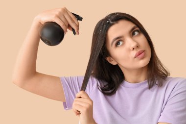 Kepek sorunu olan genç bir kadın bej arka planda saç spreyi kullanıyor.