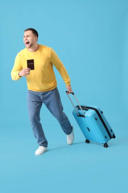 Mavi arka planda bavulu ve pasaportu olan aceleci erkek turist.