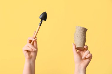 Sarı arka planda kürek ve turba kapları olan kadın elleri, yakın plan.