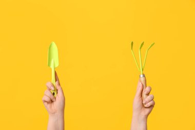 Bahçe küreği ve sarı arka planda tırmık olan kadın eller, yakın plan.