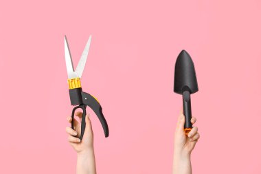 Bahçe küreği ve pembe arka planda kesiciler olan kadın eller, yakın plan.