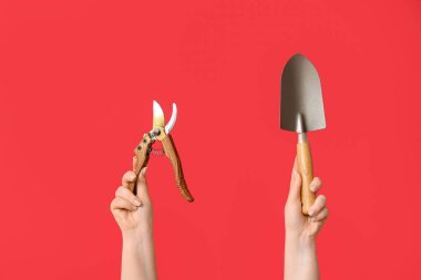 Bahçe işleriyle uğraşan kadın eller ve kırmızı arka planda kürek.