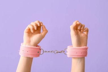 Leylak arka planında seks dükkanından pembe kelepçeli kadın elleri, yakın plan