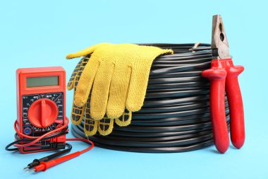 Çoklu metre, elektrik kablosu makarası, renk arka planında pense ve eldiven.