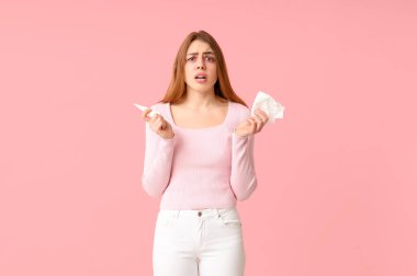 Burun spreyi ve peçeteli bir kadın pembe arka planda alerji yüzünden acı çekiyor.