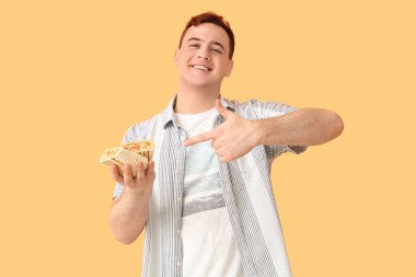 Genç adam gülümsüyor ve bej arka plandaki donör kebabına işaret ediyor.