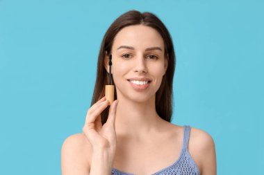 Mavi arka planda rimel fırçası olan güzel genç bir kadın.