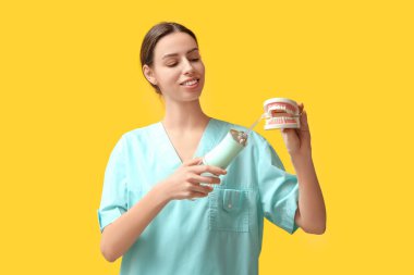 Sarı arka planda ağız sulandırıcı ve çene modeline sahip kadın dişçi