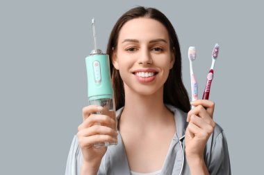 Gri arka planda diş fırçası ve ağız sulandırıcısı olan güzel bir genç kadın.