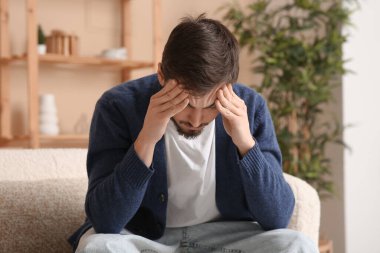 Başı ağrıyan yorgun genç adam evdeki kanepede oturuyor.