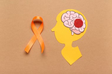 Kağıt insan kafası ve kahverengi arka planda turuncu kurdele. Çoklu Skleroz Farkındalık Ayı