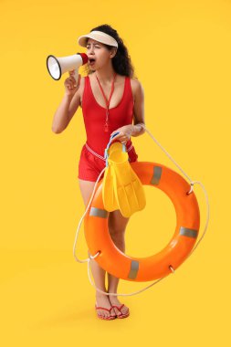 Güzel, genç, afro-amerikan kadın cankurtaran yüzgeçleri, halka şamandırası ve sarı arka planda megafonu var.