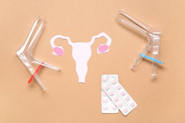 Jinekolojik spekülasyonlu kağıt rahim ve kahverengi arka planda haplar.