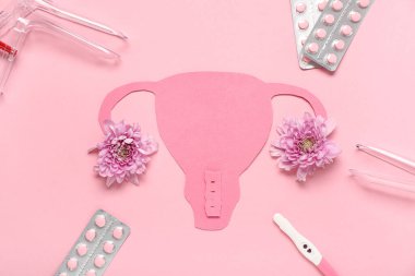 Pembe arka planda jinekolojik spekülasyon, hap, hamilelik testi ve kasımpatı çiçekli kağıt uterus.