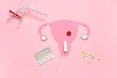 Jinekolojik spekulumlu kağıt rahim, pembe arka planda tampon ve haplar.