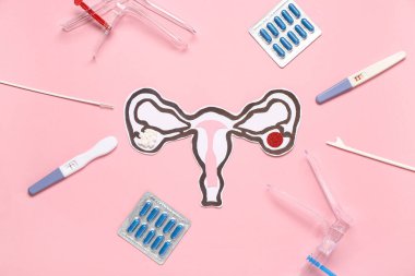 Pembe arka planda jinekolojik spekulum, hap ve pap smear test araçları içeren kağıt rahim.