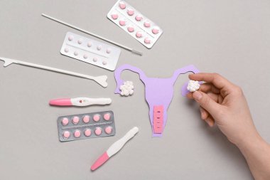 Kağıttan rahmi olan kadın eli, hamilelik testleri ve gri arka planda haplar.