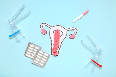 Mavi arka planda jinekolojik spekulumlu kağıt rahim, haplar ve hamilelik testi.