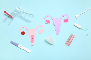 Jinekolojik spekulumlu kağıt uteruslar, mavi arka planda haplar ve hamilelik testi.