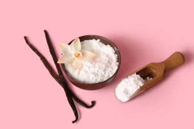 Bir kase vanilya tozu ve pembe arka planda çubuklar.