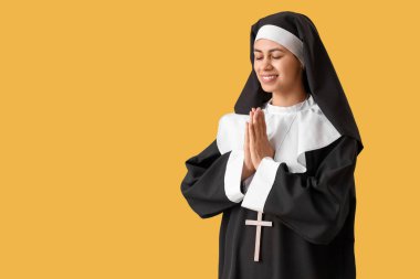 Genç rahibe sarı arka planda dua ediyor.