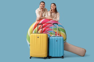 Güzel, genç, mutlu, bavulları ve mavi arka planda şişme yatağı olan bir çift turist.